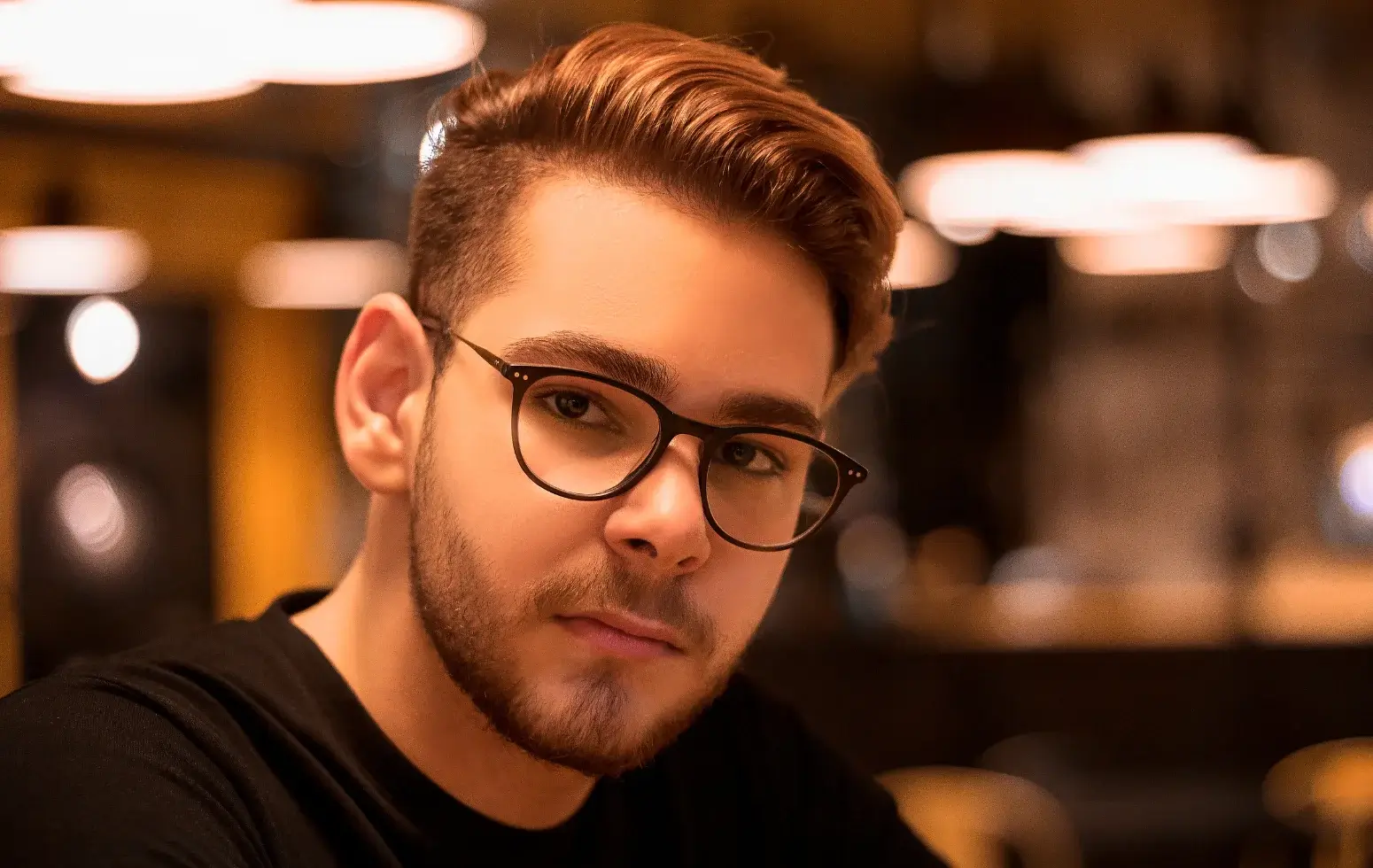 młody meżczyzna w okularach, z brodą, jasnymi, krótkimi włosami z zakolami